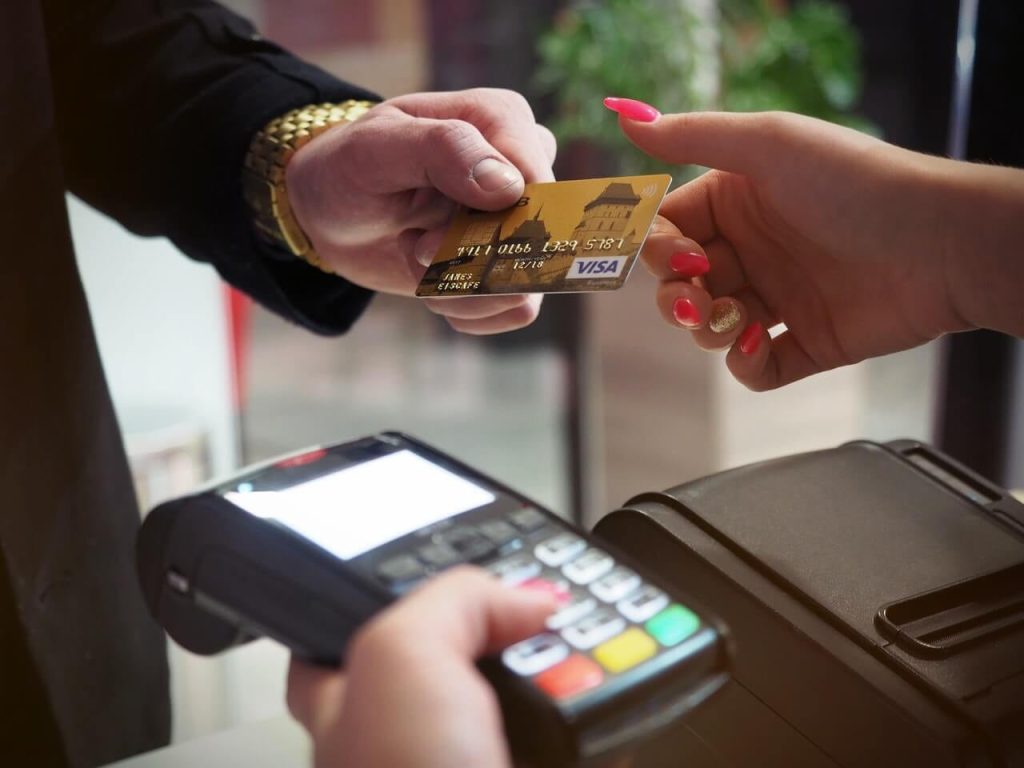 picture of a man's hand giving a credit card to a woman with a credit card machine in the other hand