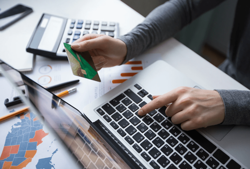 picture of hand holding credit card while other hand types on laptop